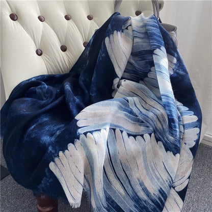 Oversized galaxy ocean wool wrap arranged on a tufted chair with flowing ivory wave motifs