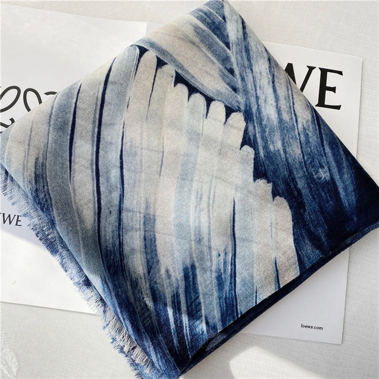 Folded blue and ivory ocean wave wool scarf displayed on a fashion magazine