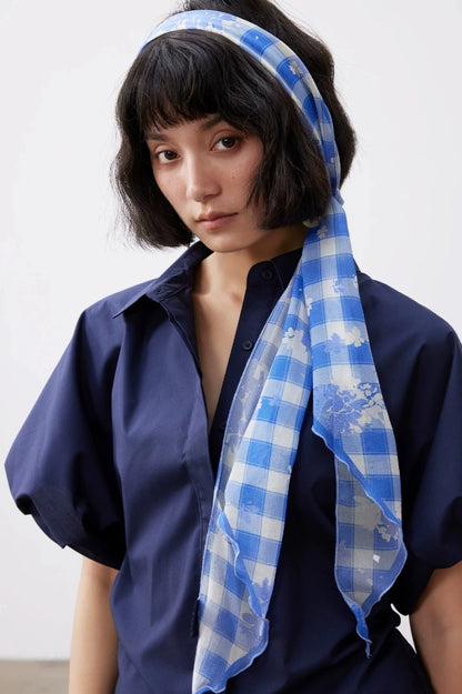Blue and white plaid silk headband scarf styled in the hair with a long flowing silhouette.