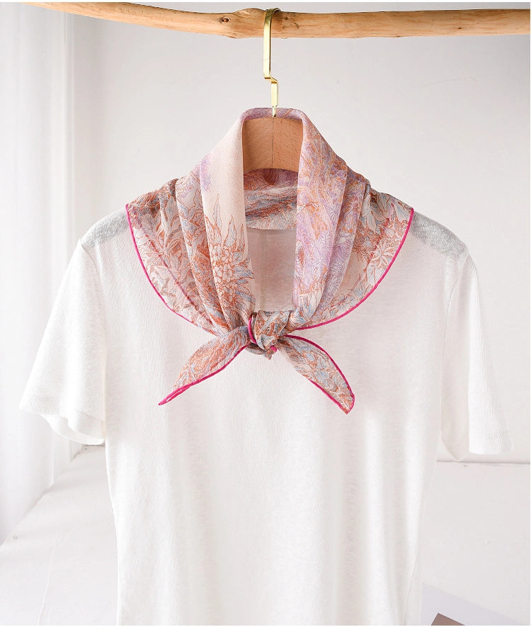 Pink silk square scarf tied neatly at the neck with botanical garden print