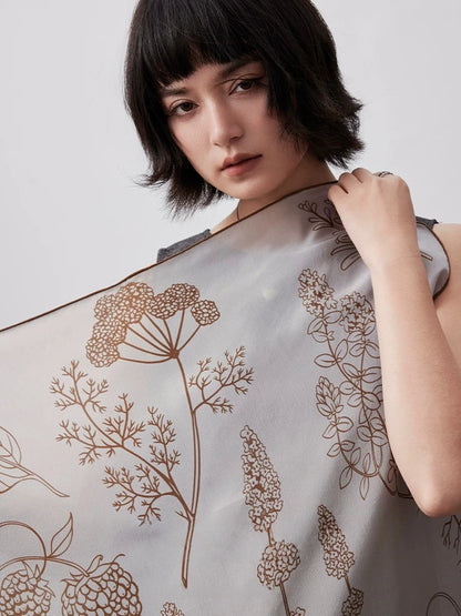 Botanical mulberry silk square scarf styled over the shoulder, featuring refined floral line art in neutral tones