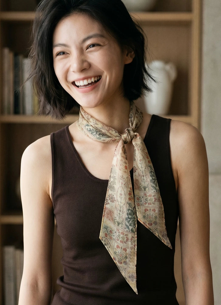 Woman wearing a brown floral mulberry silk skinny scarf tied loosely at the neck with a dark brown top