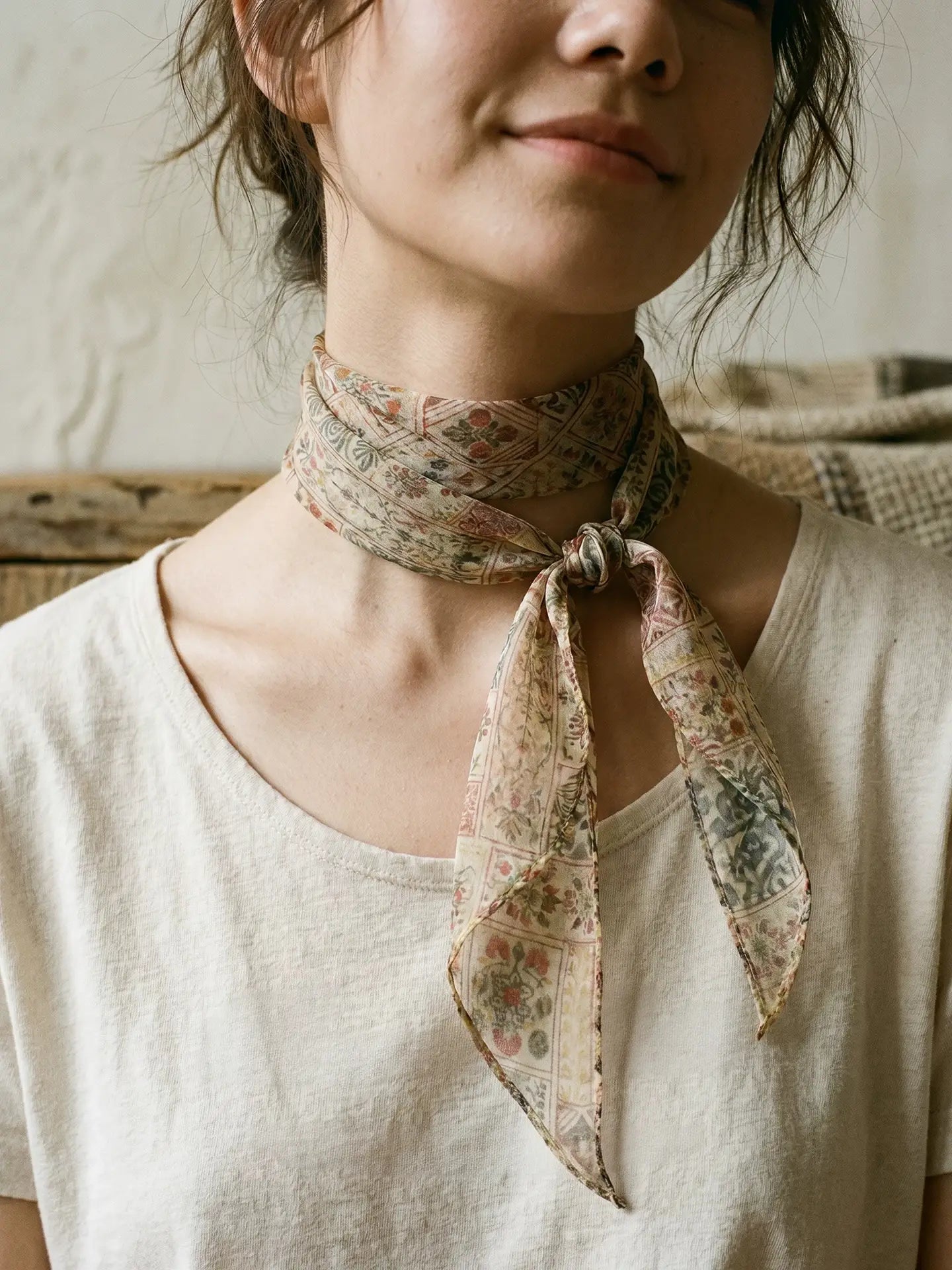 Close-up of a brown vintage floral mulberry silk scarf tied at the neck over a cream linen top