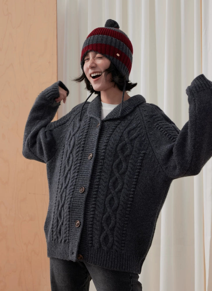 Model wearing a burgundy and charcoal grey striped wool earflap beanie with a grey cable-knit cardigan.