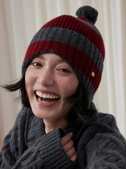 Front close-up of a smiling model wearing a burgundy and charcoal grey striped wool earflap beanie.