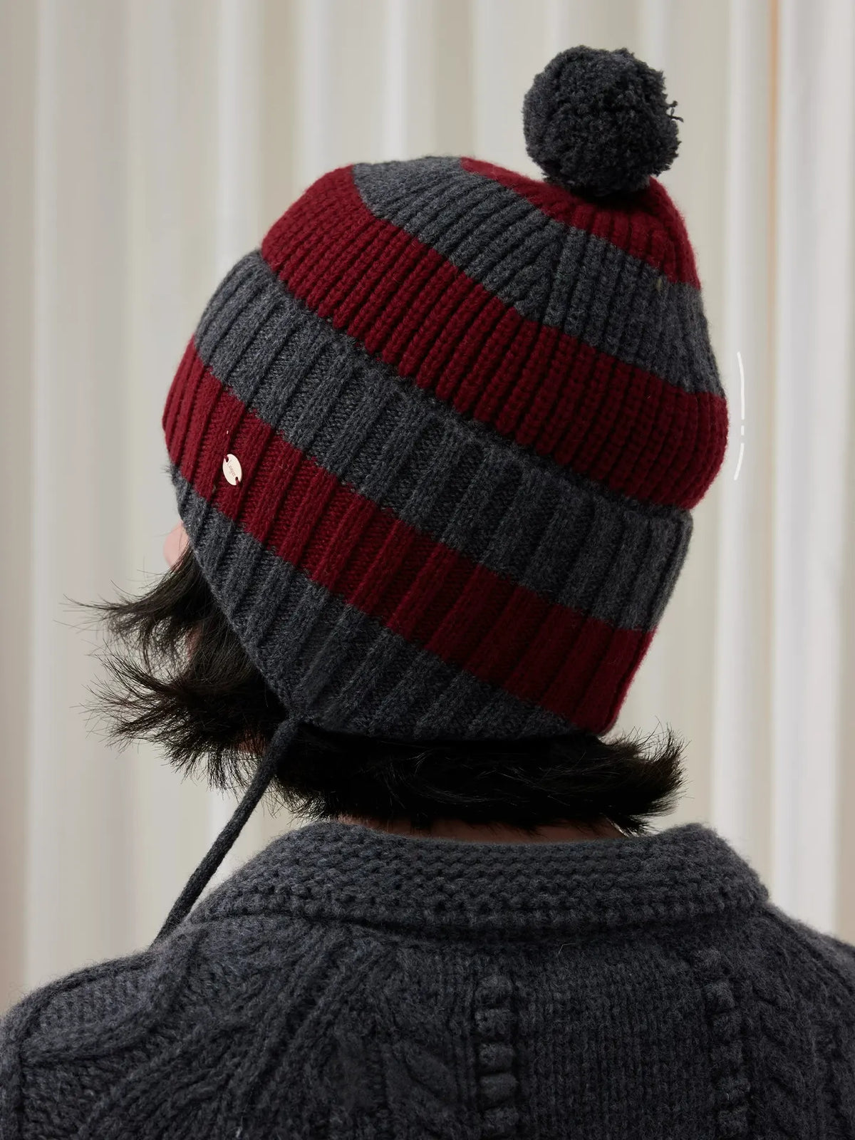 Rear view of a burgundy and charcoal grey striped wool beanie, showing the ribbed knit and grey pom pom.