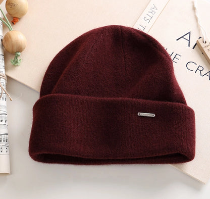 Burgundy pure cashmere cuffed beanie with a small metal accent in a minimalist flat lay