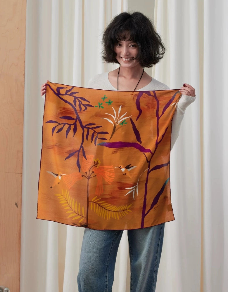 Woman holding open a burnt orange mulberry silk square scarf with purple branches and delicate botanical details