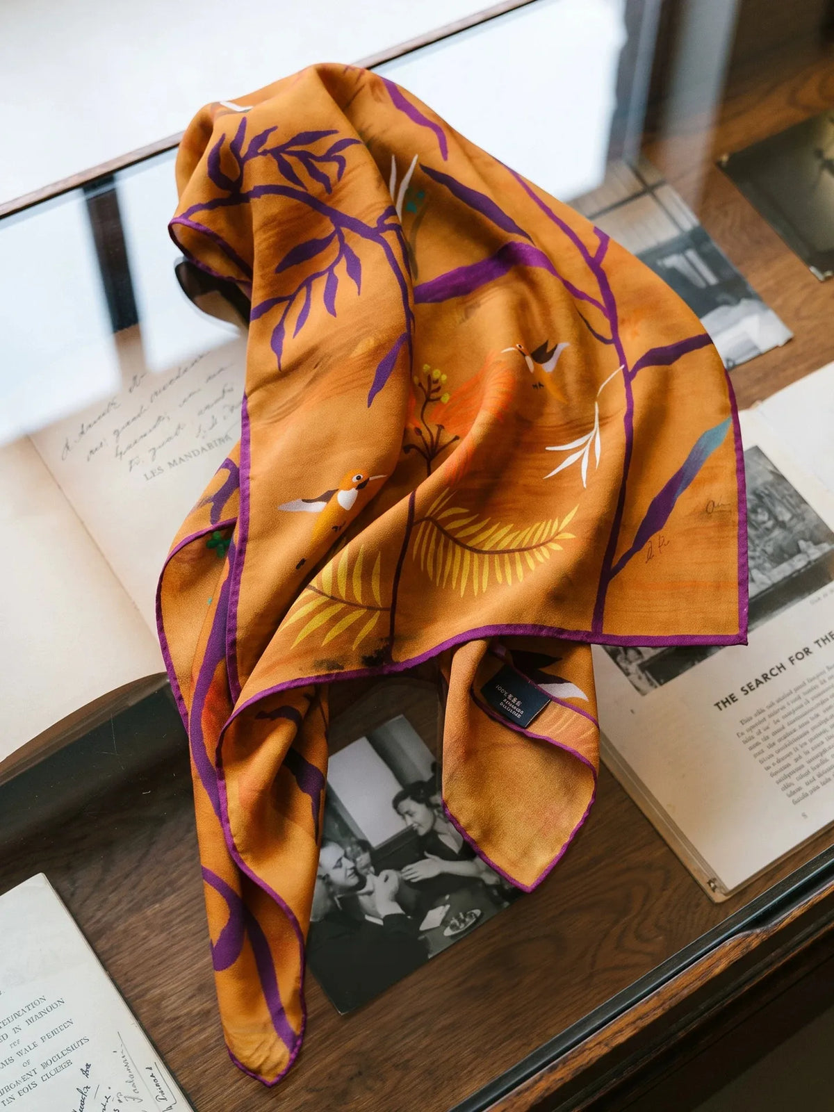 Burnt orange abstract botanical mulberry silk scarf draped over an open magazine on a wooden table