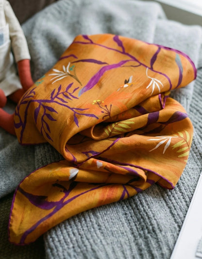 Close-up of a burnt orange mulberry silk scarf softly folded to show purple branches and lustrous fabric