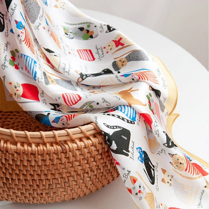 Artistic cat print silk square scarf styled with a woven bag for a refined everyday accessory look.