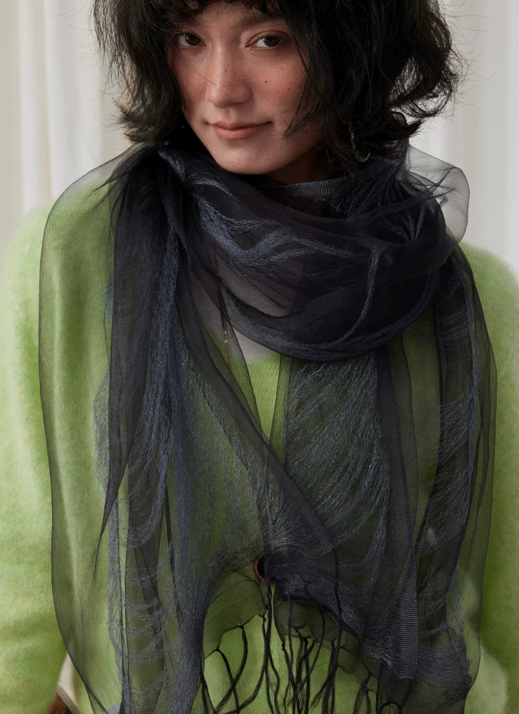 Close-up of a charcoal gray mulberry silk fringe scarf layered over green knitwear
