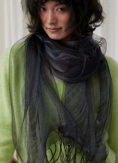 Close-up of a charcoal gray mulberry silk fringe scarf layered over green knitwear