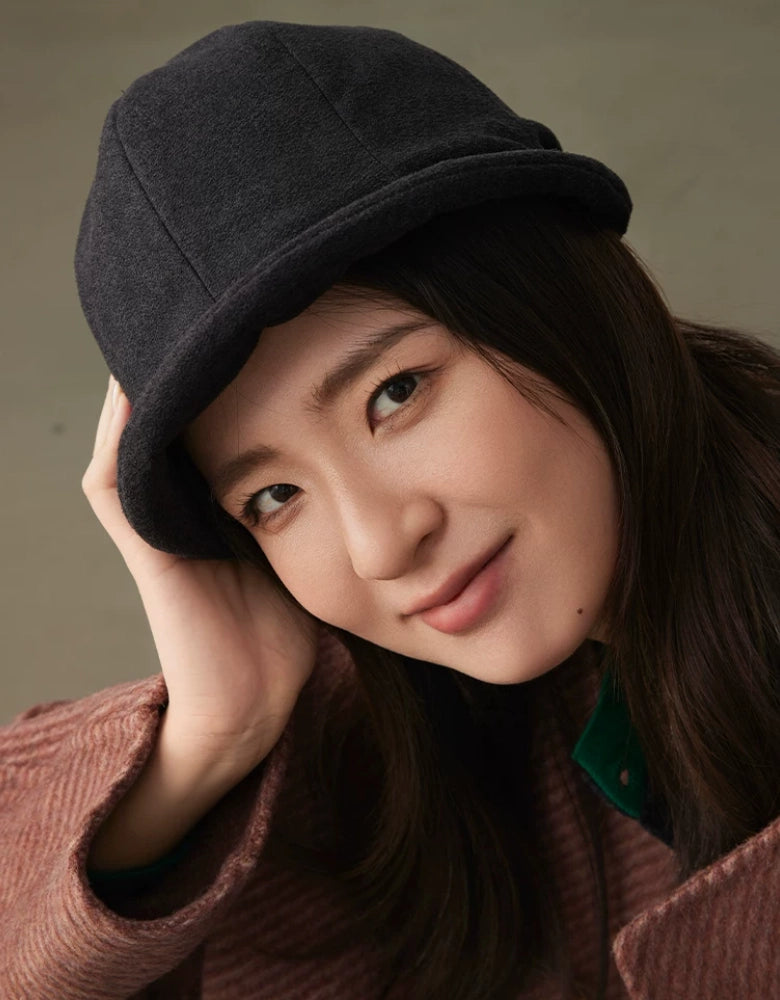 Close-up of a woman styling a charcoal gray felt cloche hat with a softly rolled brim