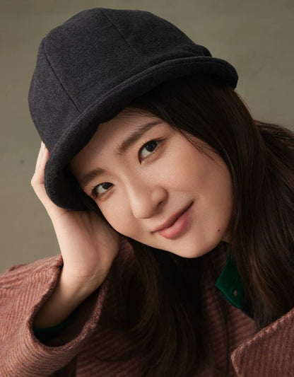 Close-up of a woman styling a charcoal gray felt cloche hat with a softly rolled brim