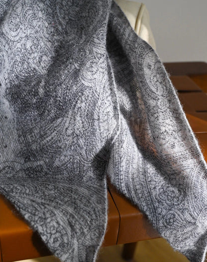 Close-up of a charcoal grey cashmere scarf showing tonal paisley motifs and a softly textured surface.