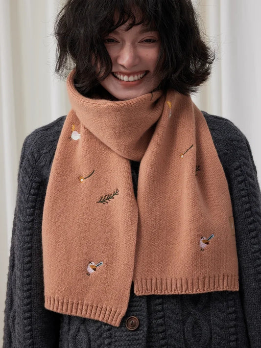 Model wearing a camel embroidered wool scarf with bird and floral motifs over a charcoal cardigan.