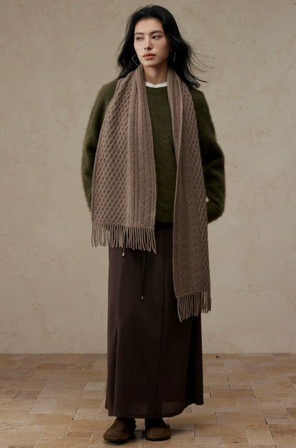 Full-length view of a model wearing a long coffee brown cable knit scarf with fringed ends.