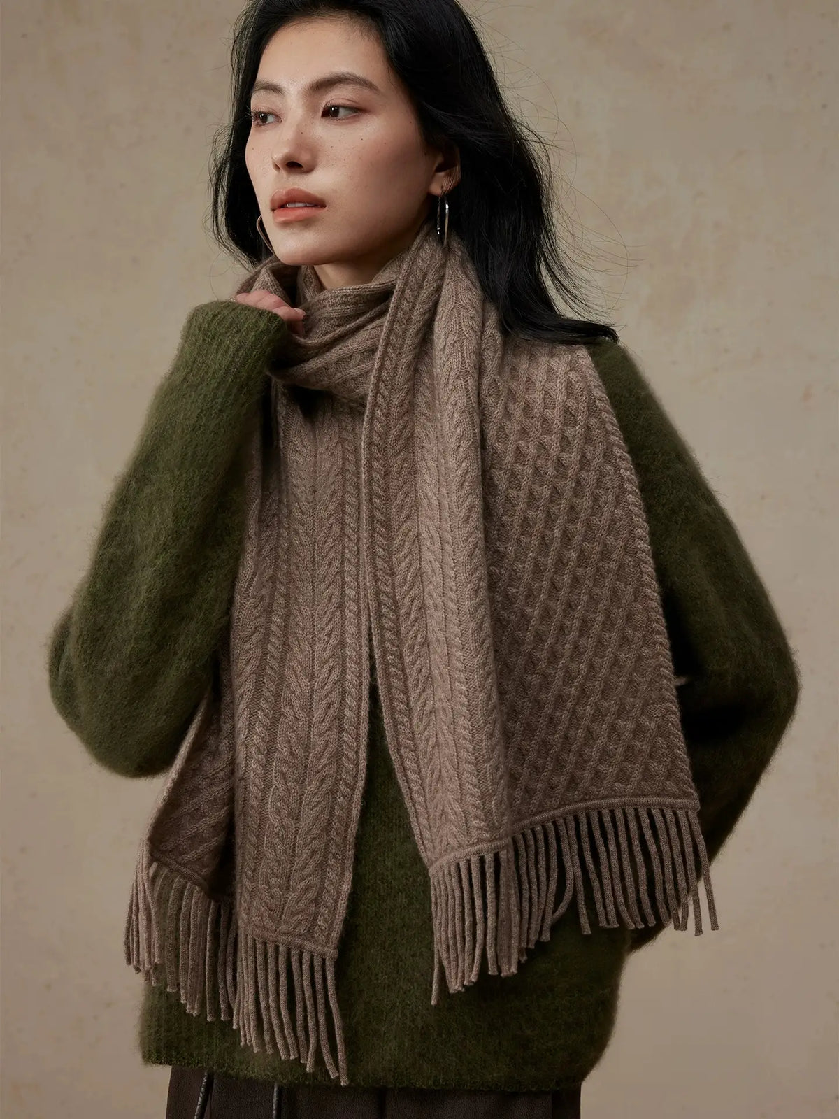 Angled view of a model wearing a coffee brown cable knit scarf wrapped at the neck, with fringed ends.