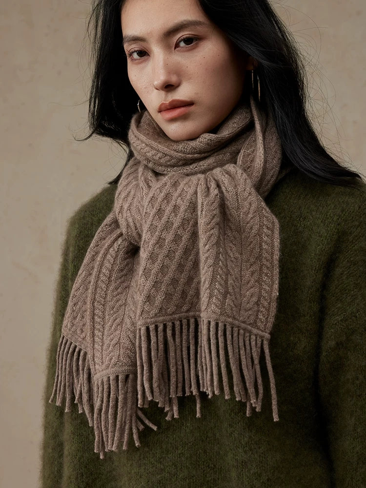 Close-up of a coffee brown cable knit scarf looped around the neck, showing the knit pattern and fringe.