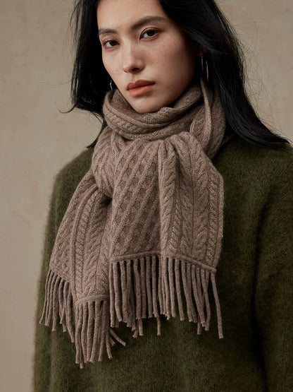 Close-up of a coffee brown cable knit scarf looped around the neck, showing the knit pattern and fringe.