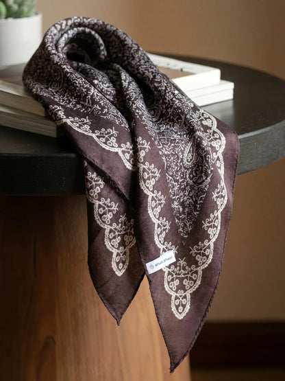 Coffee brown silk wool triangle scarf draped over a wooden table to show its floral border