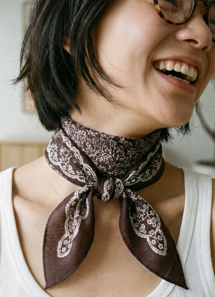 Woman styling a coffee brown floral silk wool scarf as a softly knotted neckerchief
