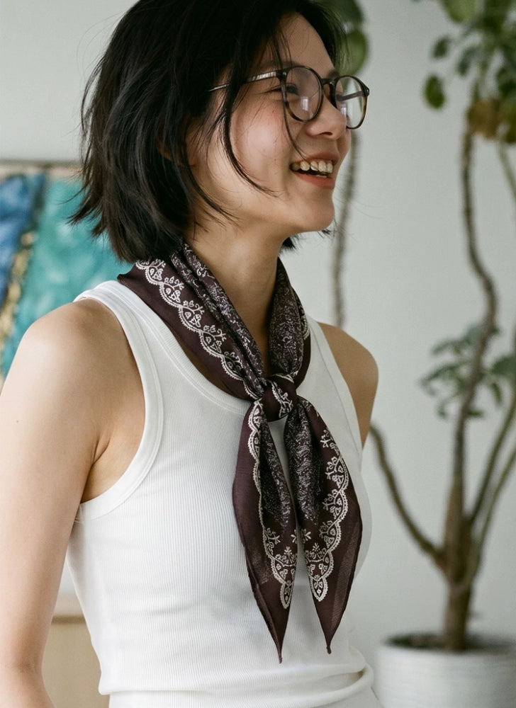 Woman wearing a long coffee brown silk wool neck scarf with an ivory sleeveless top