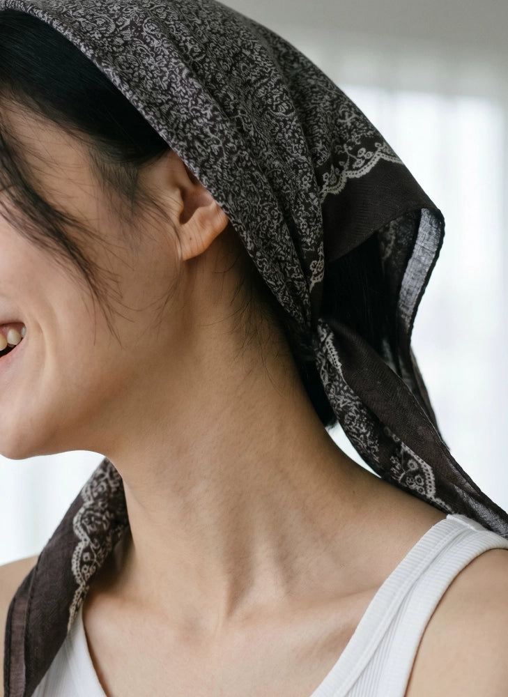 Woman styling a coffee brown silk wool triangle scarf as a vintage floral headscarf