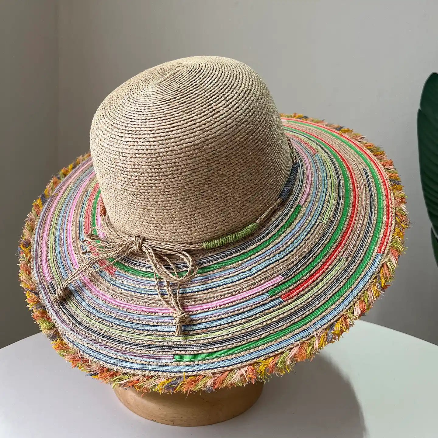 Top view of beige raffia wide brim sun hat with colorful striped brim and frayed edge.