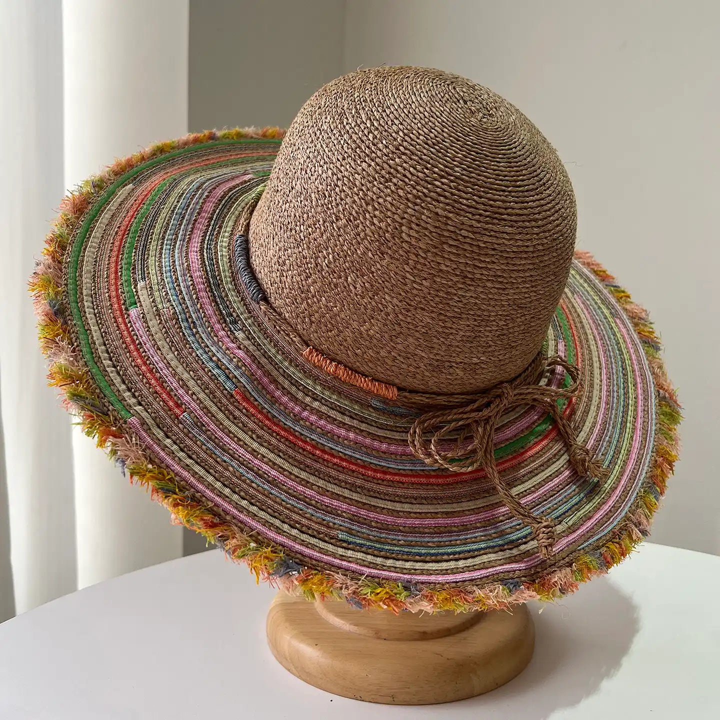Top view of brown raffia sun hat with colorful wide brim and frayed edge detail.
