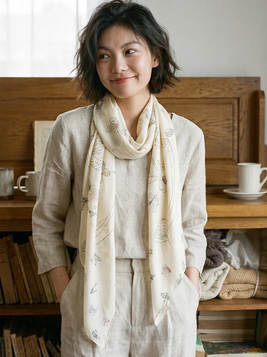 Model wearing a cream printed silk scarf in a loose neck loop, with both ends falling over an ivory suit.