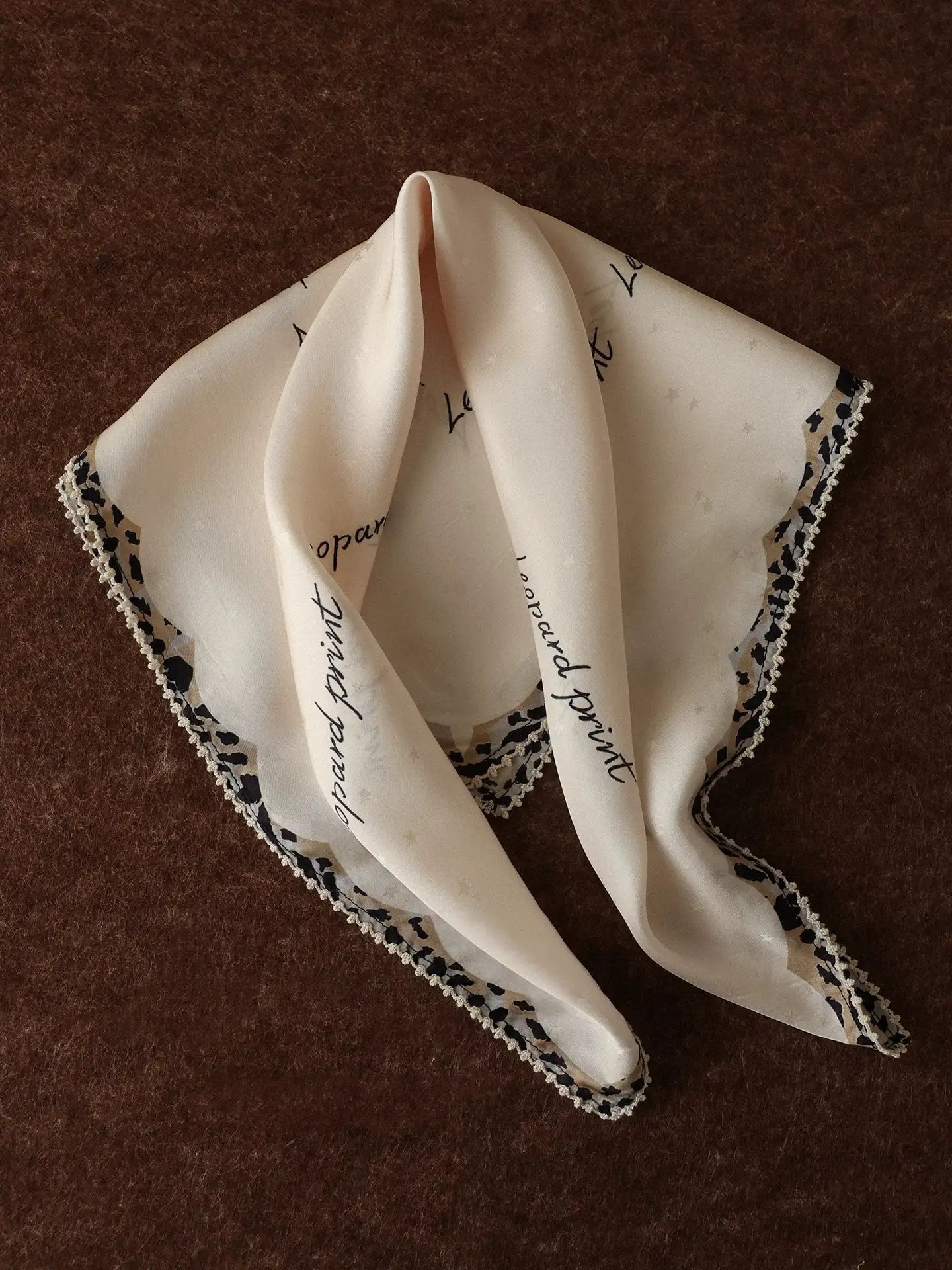 Creamy ivory mulberry silk square scarf with leopard trim folded on a brown background