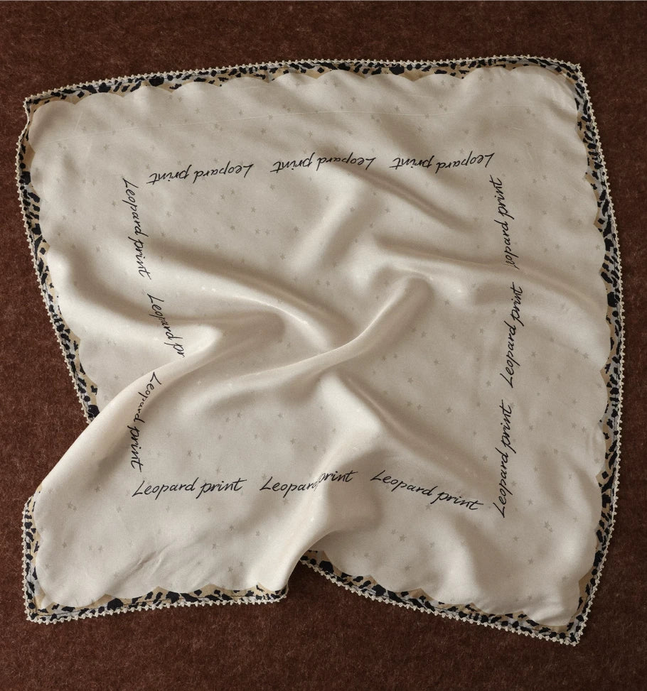 Creamy ivory silk square scarf with cursive script and leopard-print border displayed flat
