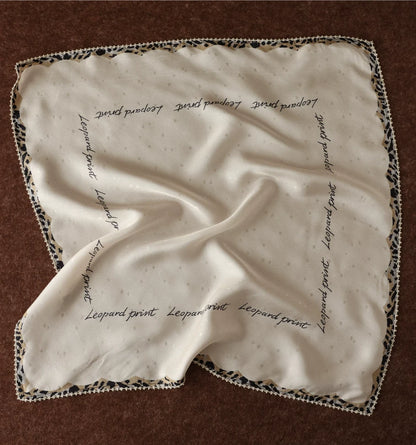 Creamy ivory silk square scarf with cursive script and leopard-print border displayed flat