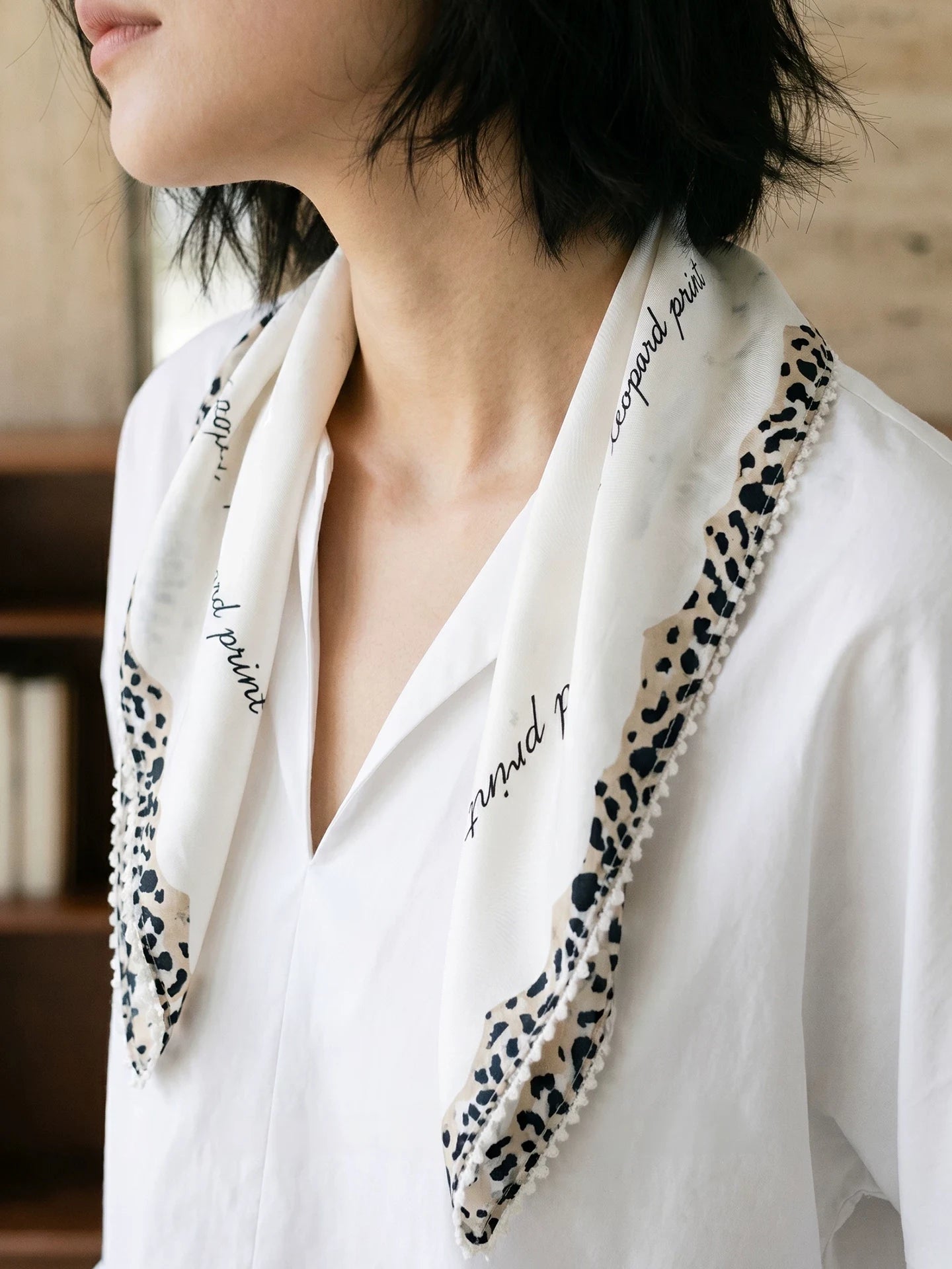 Woman wearing a creamy ivory leopard-trim silk scarf loosely draped over a white shirt