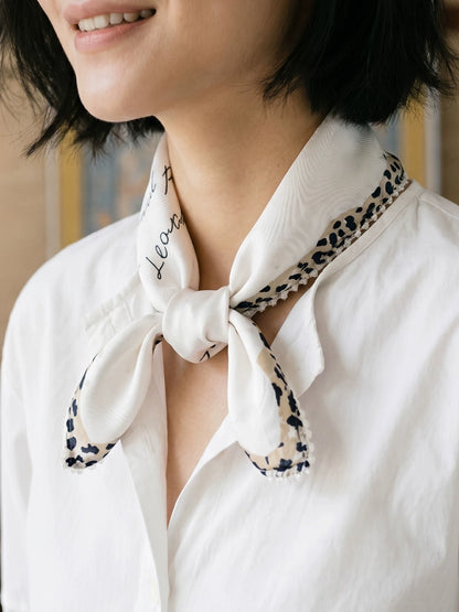 Woman styling a creamy ivory leopard-trim silk neckerchief with a white button-down shirt