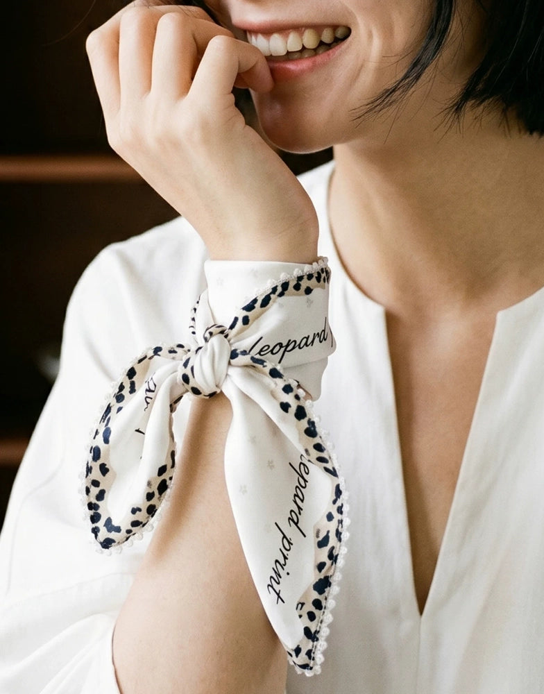 Creamy ivory silk neck scarf with leopard edging styled in a soft bow knot