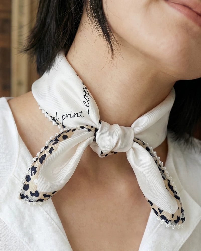 Close-up of a creamy ivory mulberry silk neckerchief with cursive script and leopard trim