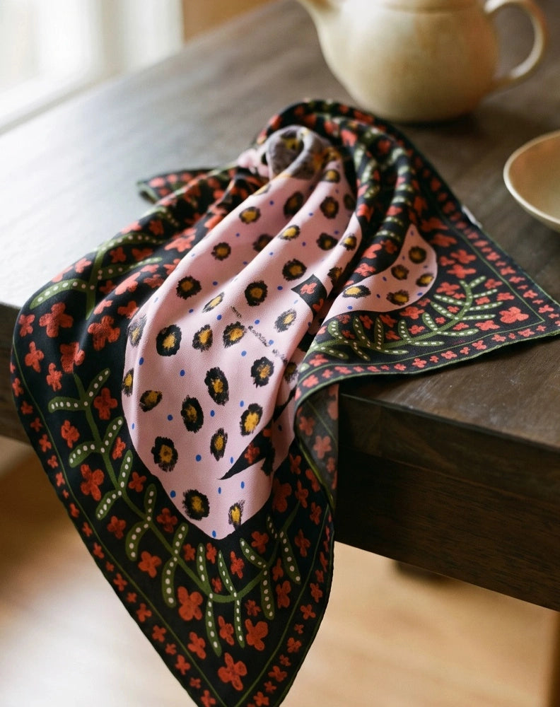 Crimson leopard floral mulberry silk scarf draped beside a cup on a wooden table