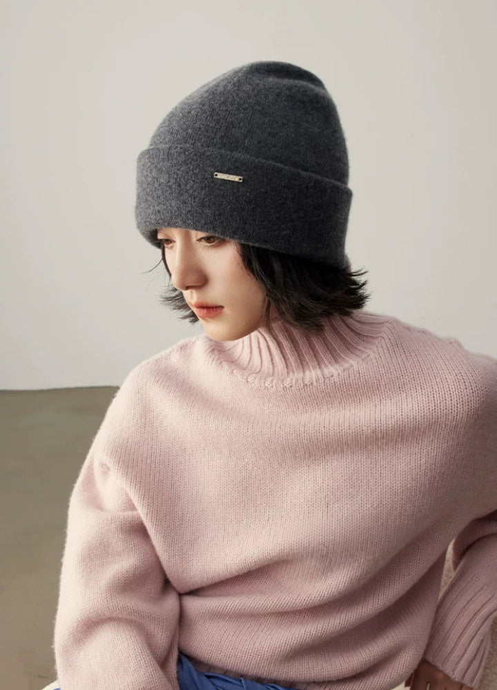 Seated model styling a dark gray 100% cashmere cuffed beanie with a pink sweater