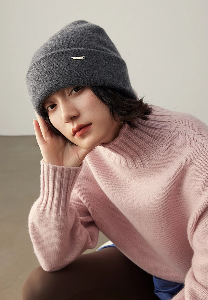 Woman in a pink sweater wearing a dark gray cashmere winter beanie in a relaxed pose