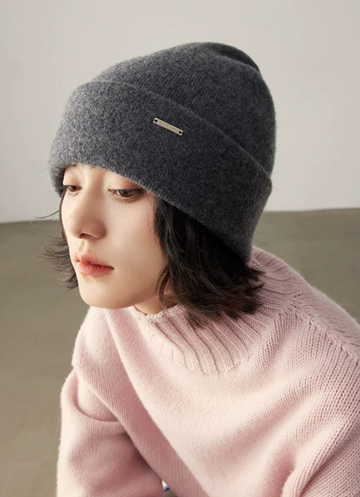 Close-up of a woman wearing a dark gray pure cashmere cuffed beanie with a pink knit top