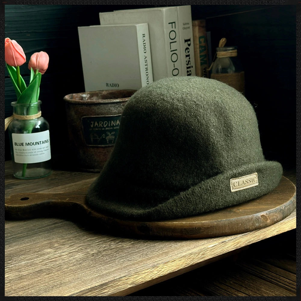 Side view of a dark green rolled brim wool cloche hat displayed with books and flowers
