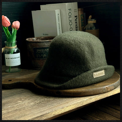 Side view of a dark green rolled brim wool cloche hat displayed with books and flowers