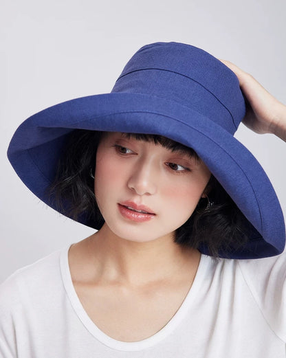 Woman adjusting a deep blue packable sun hat with a flexible wrap-around brim