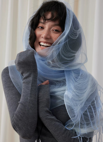 Woman styling a sheer mountain blue silk scarf as a soft hood and shoulder wrap