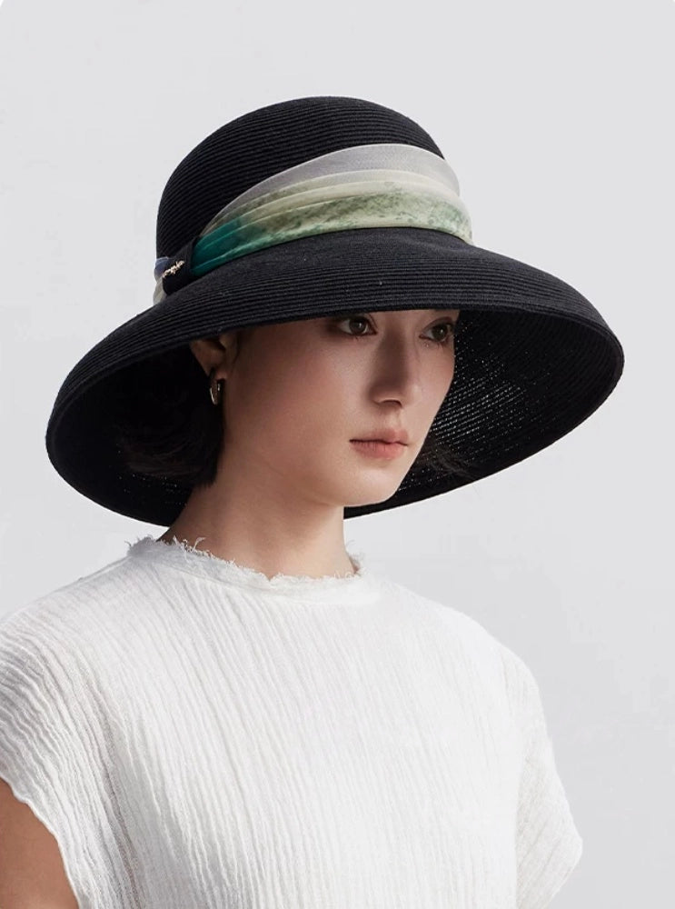 Woman wearing elegant black scarf ribbon wide brim sun hat with white summer top.