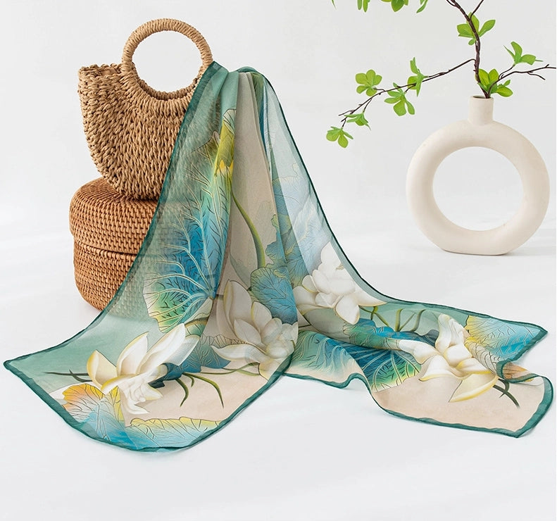 Floral lotus long silk scarf with light green tones styled beside a woven handbag