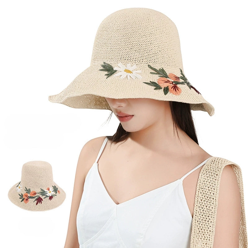 Woman wearing an ivory floral embroidered straw sun hat with wide brim and matching woven shoulder bag for summer vacation style